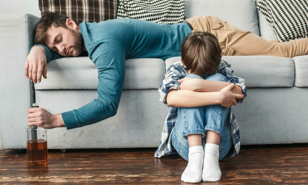 little boy crying next to passed out father